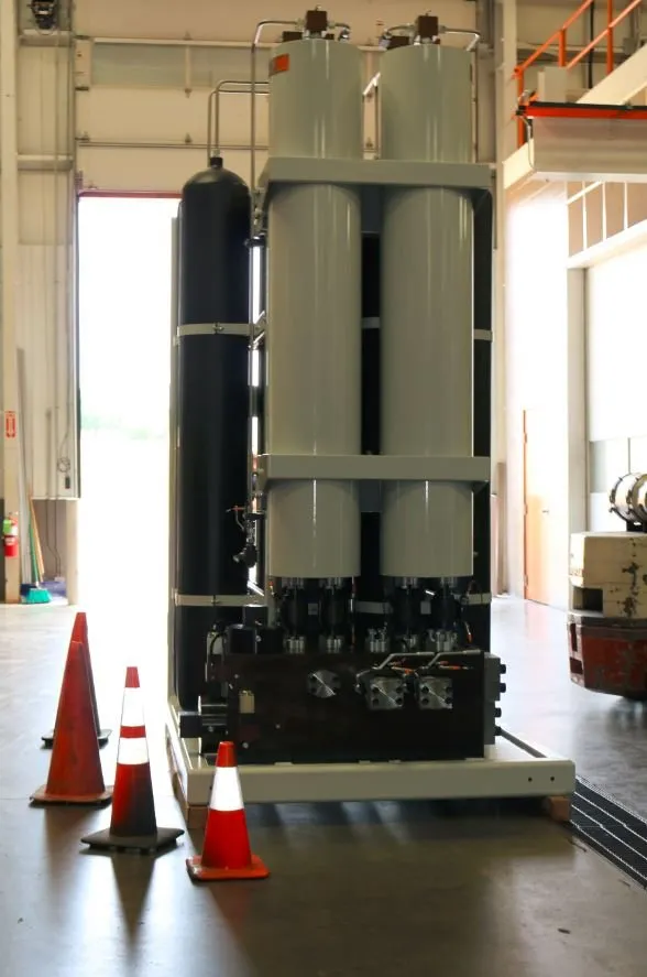 Front view of two large cylindrical accumulators on a steel frame, with safety cones near an open bay door