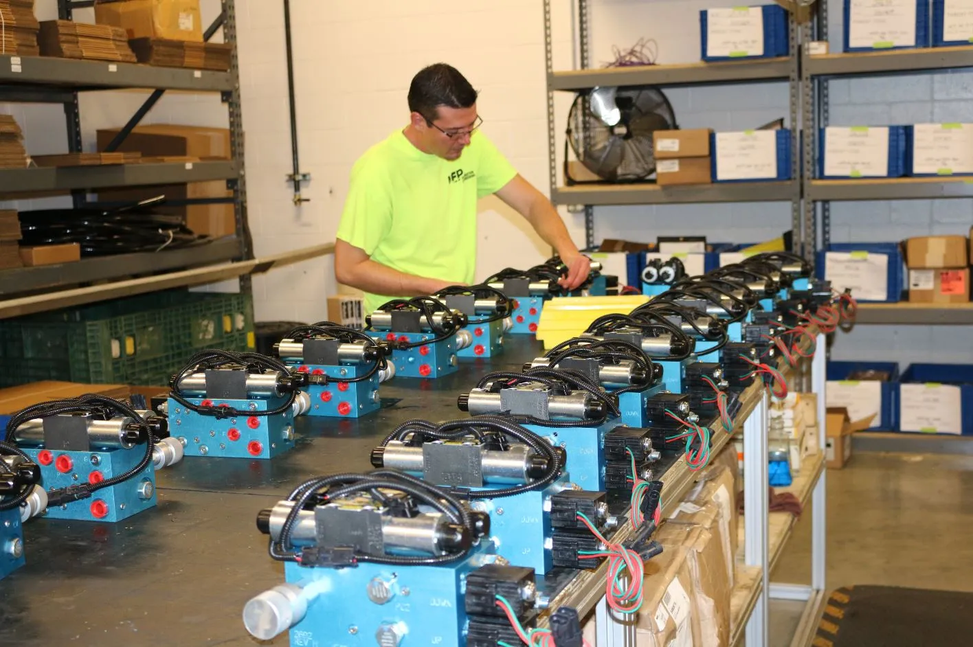 MFP technician wiring a row of compact blue hydraulic valve assemblies on an assembly bench