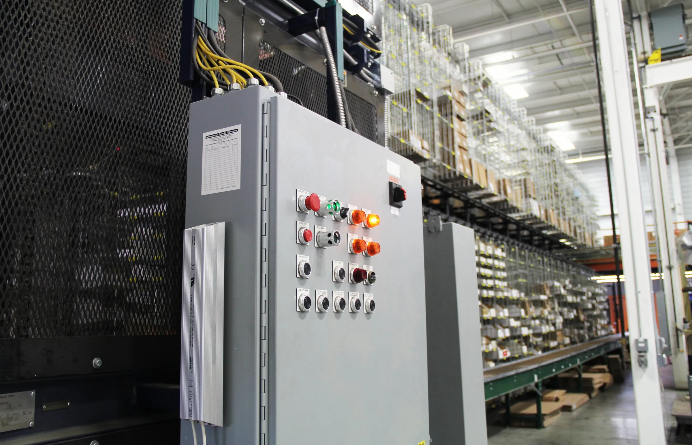 Control panel with pushbuttons mounted beside warehouse shelving and a conveyor