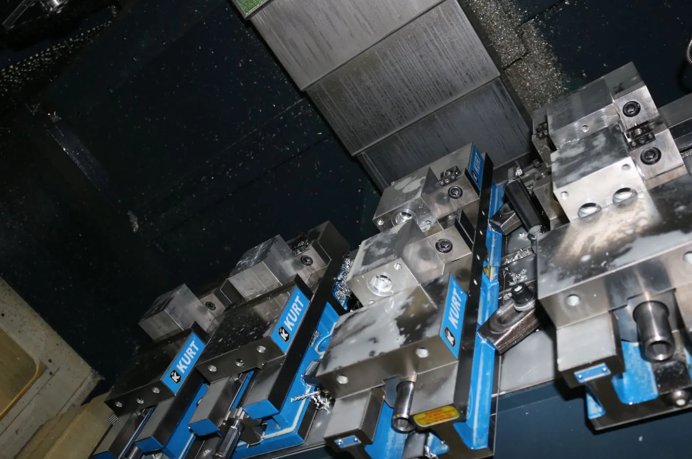 Aluminum blocks clamped in blue Kurt vises on a CNC machine table, dusted with metal shavings