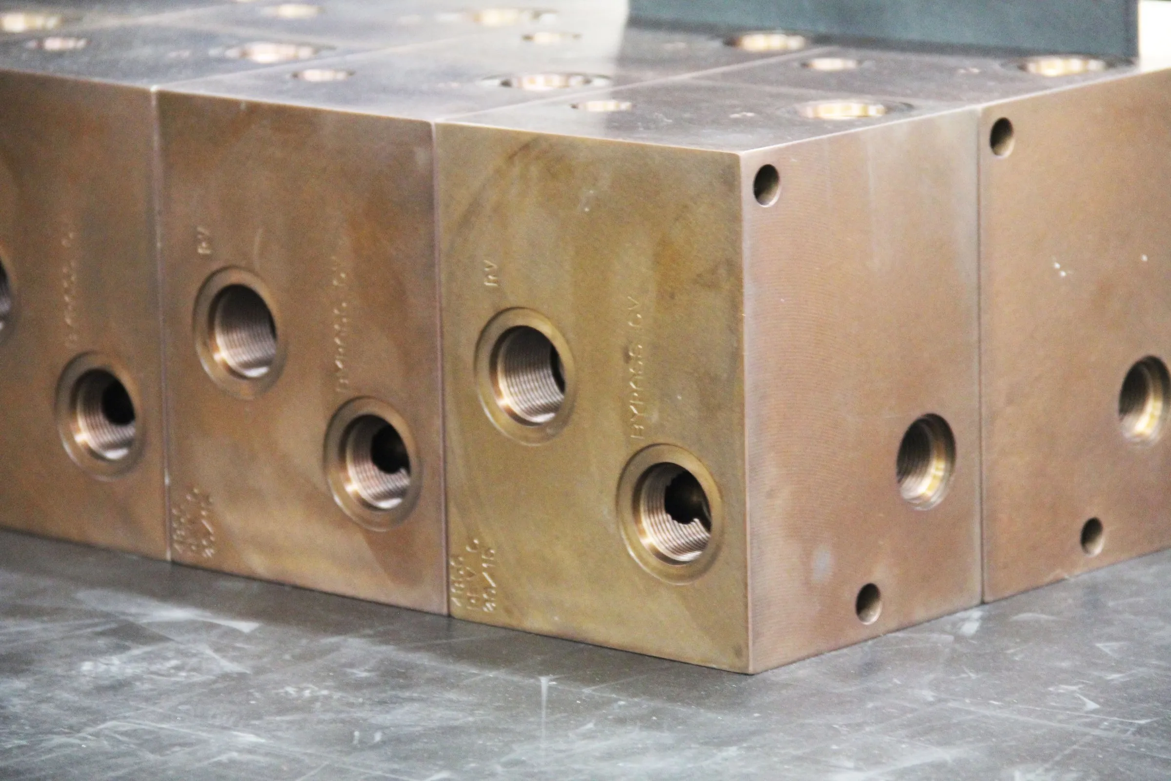 Two machined hydraulic manifold blocks with drilled ports on a steel table