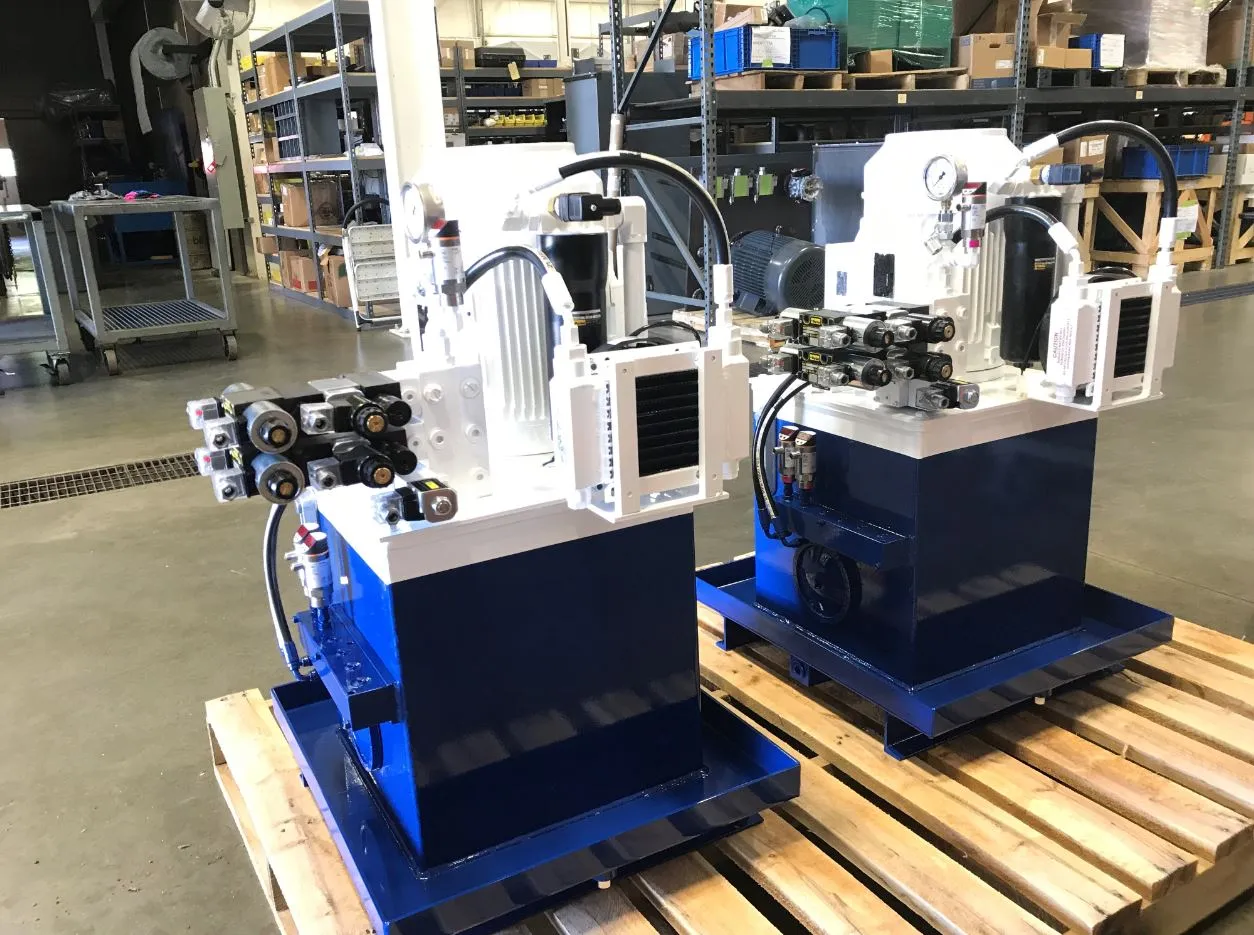 Two hydraulic power units with blue reservoirs and machined valve stacks, staged on wooden pallets
