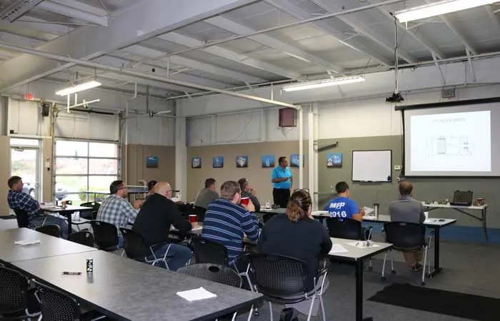 Instructor teaches a cylinder-parts diagram to a seated class in a training room