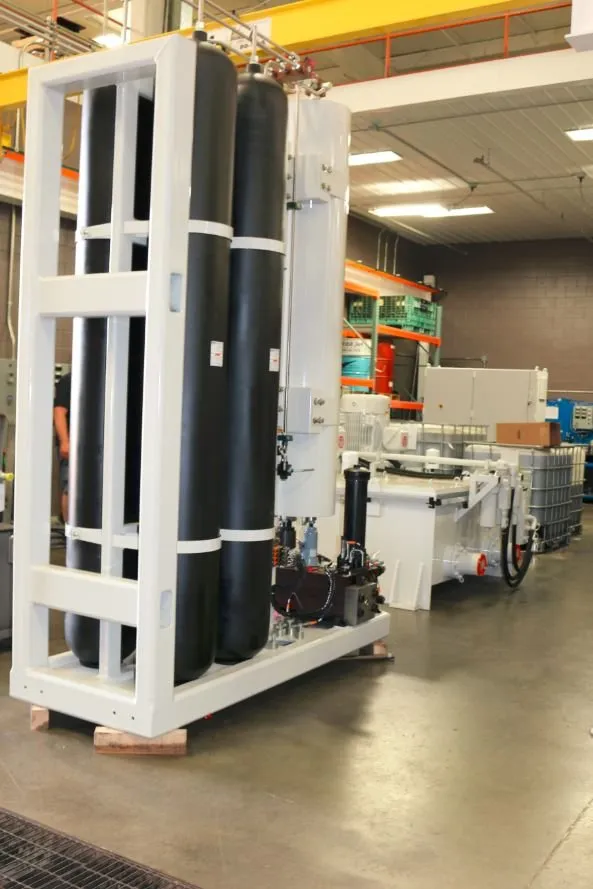 Rack holding two large black cylinders on a pallet, next to a hydraulic reservoir with bronze motors in a warehouse