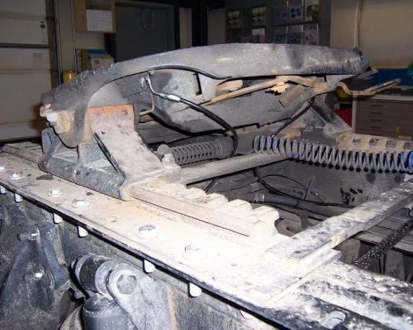 Close-up of a dusty leaf-spring suspension mount and grease fitting on a truck-trailer chassis