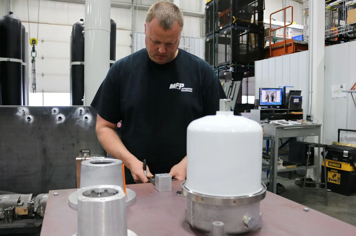 MFP technician assembling a filter housing at a workbench, black accumulator tanks behind him