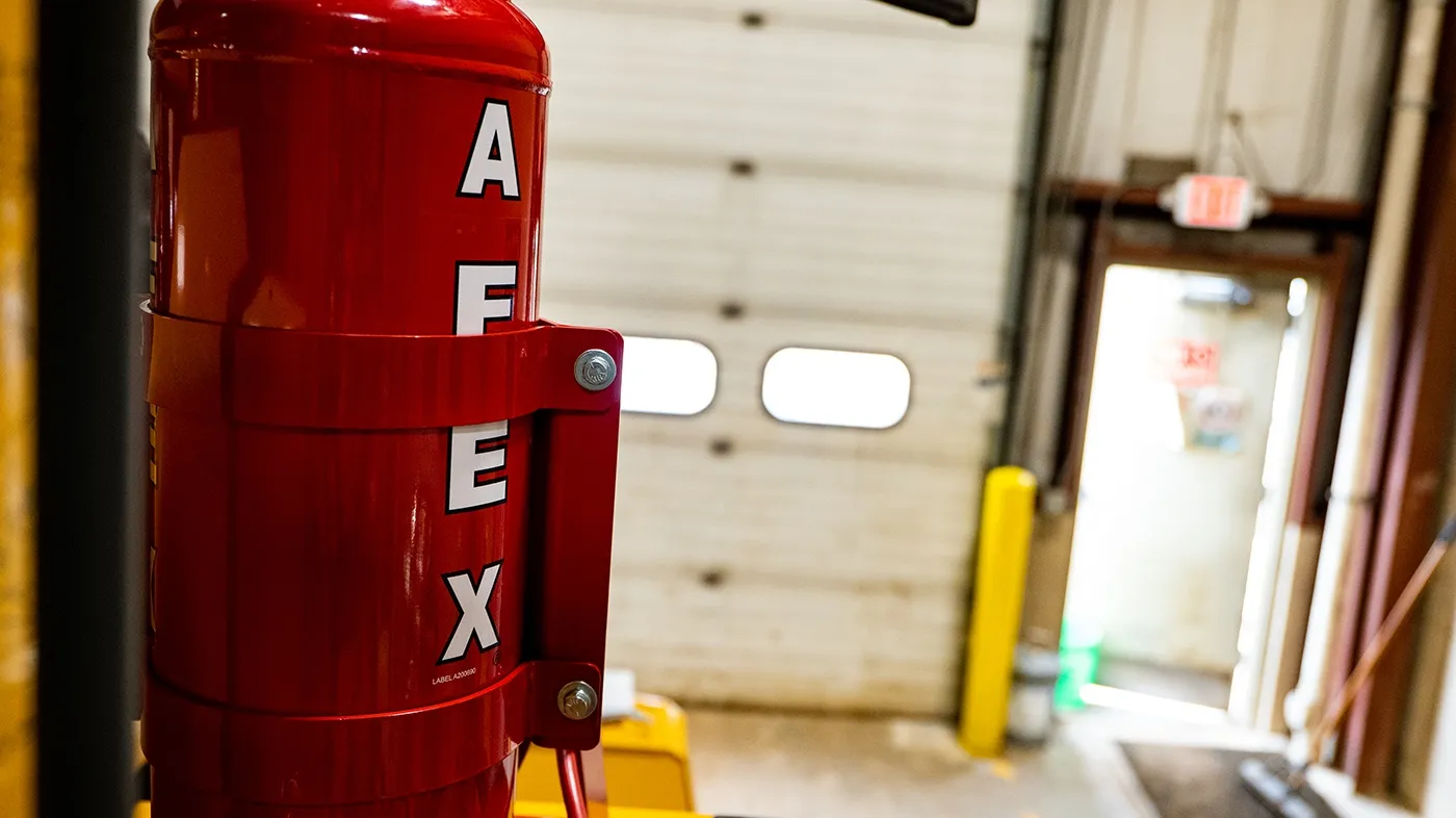 An AFEX fire suppression tank mounted on a machine, with a shop door behind it