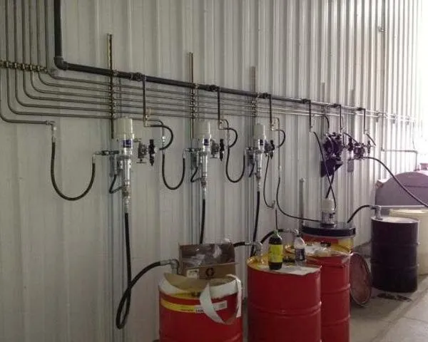 A fluid management wall with metered dispensing pumps, hose reels and red oil drums beside storage tanks
