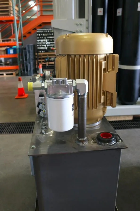A close-up of a gold electric motor and filter mounted on a stainless steel hydraulic reservoir