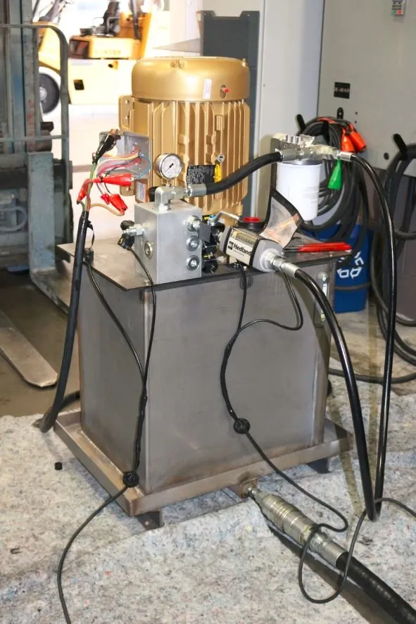 Gold-painted motor and Hedland flow meter mounted on a stainless hydraulic reservoir, with a forklift in the background