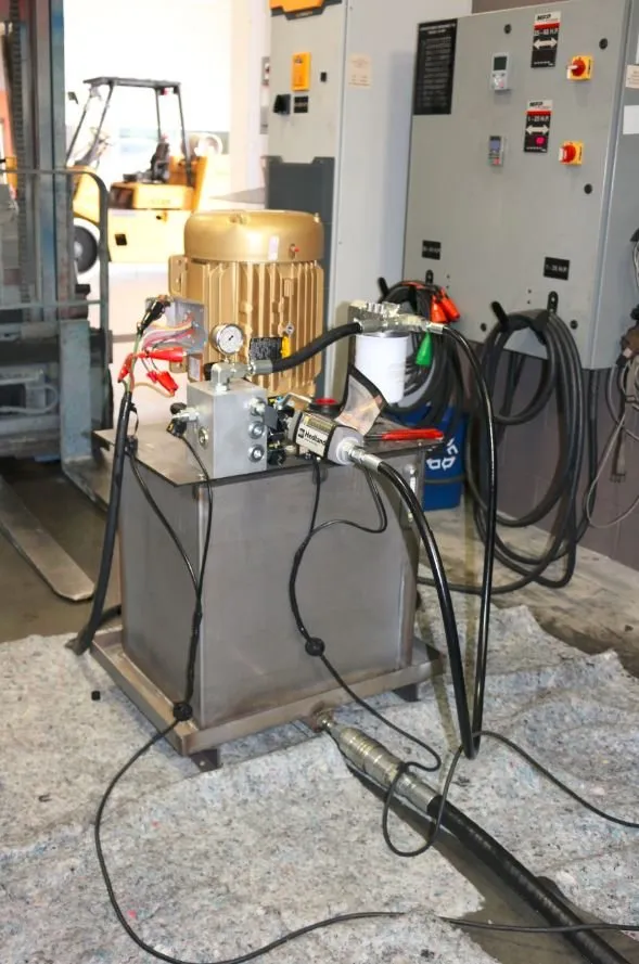 A gold electric motor on a stainless steel hydraulic reservoir, positioned near industrial control panels