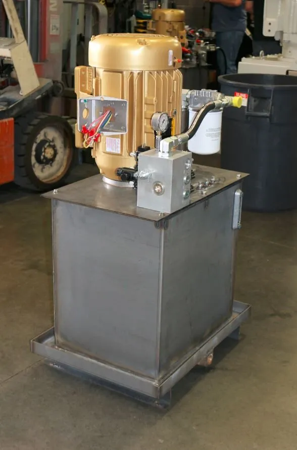 Gold-painted motor mounted on a hydraulic reservoir, with a forklift and trash can in the background