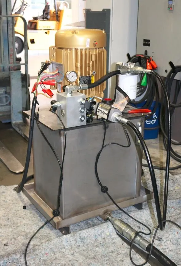 Gold-painted motor and pressure gauge mounted on a stainless hydraulic reservoir, with a Hedland flow meter attached
