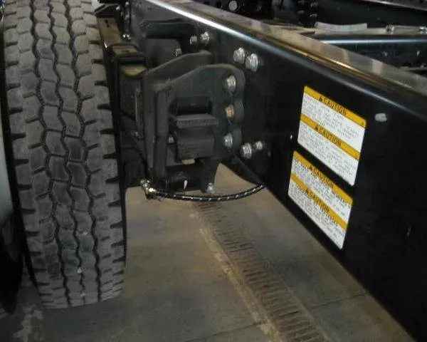 A grease line runs to an axle mount on a truck frame rail, caution stickers visible nearby