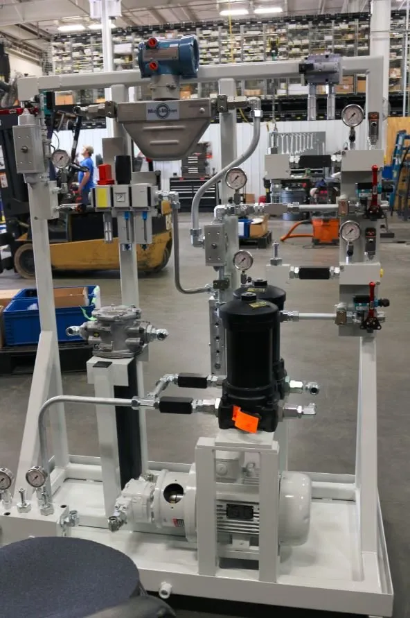 Hydraulic power unit skid with a Micro-Motion flow meter, gauges and a black filter canister, with a worker in the background