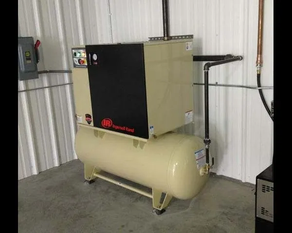 An Ingersoll Rand air compressor with a horizontal storage tank, mounted against a metal shop wall
