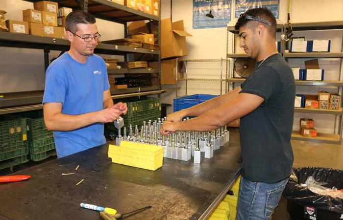 Two people sorting small metal hardware into a foam parts organizer at a workbench