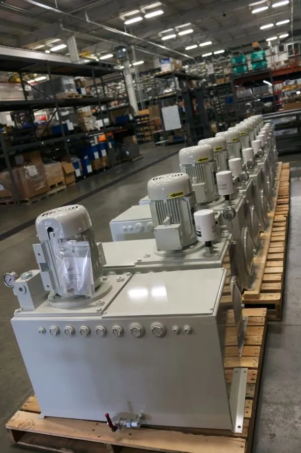 Long row of matching gray hydraulic power units lined up on pallets in a warehouse