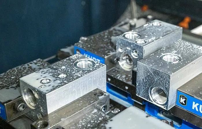 Aluminum manifold blocks being machined on a CNC mill, with coolant on the parts