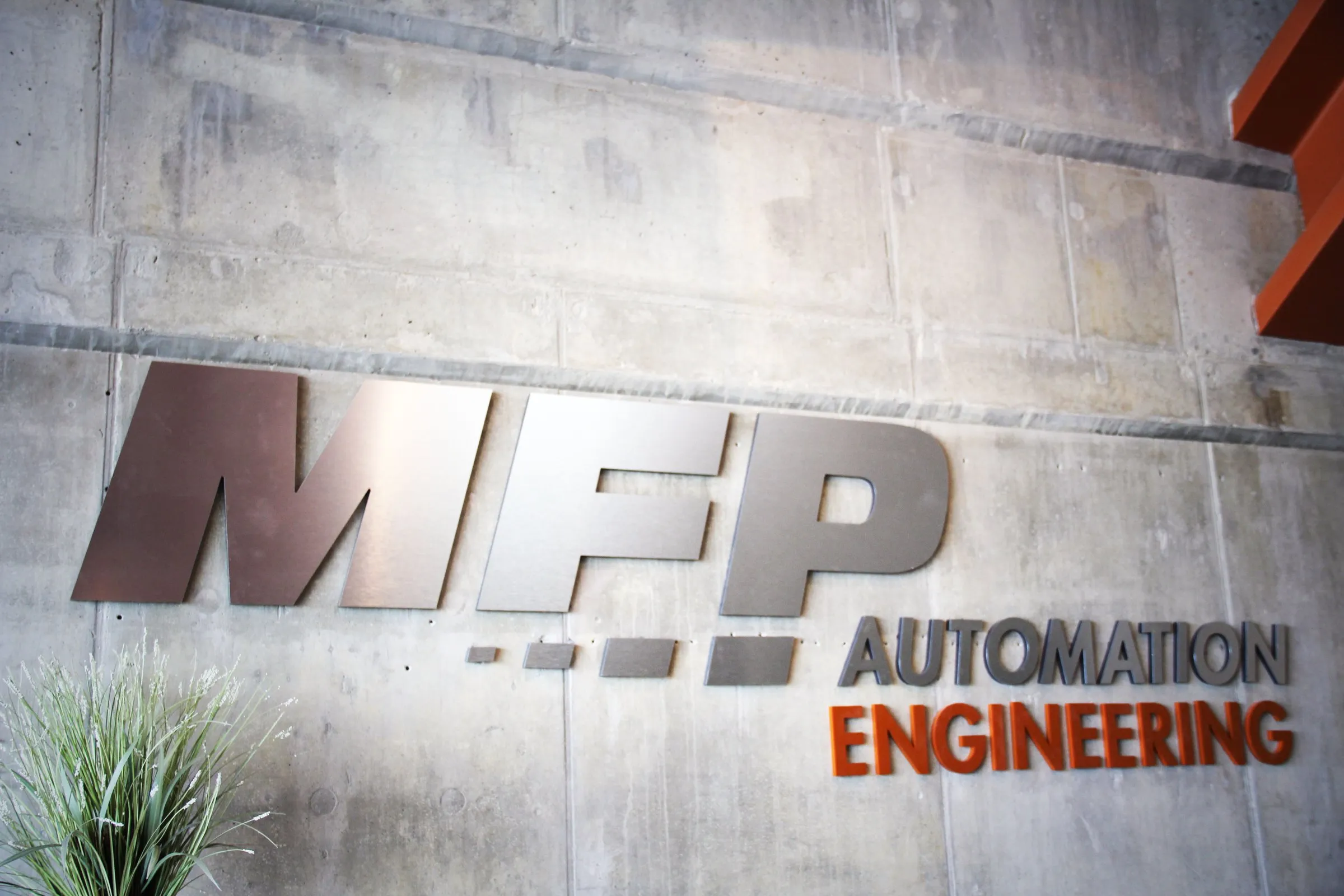 Brushed-metal MFP Automation Engineering logo on a concrete wall inside the Hudsonville, MI headquarters