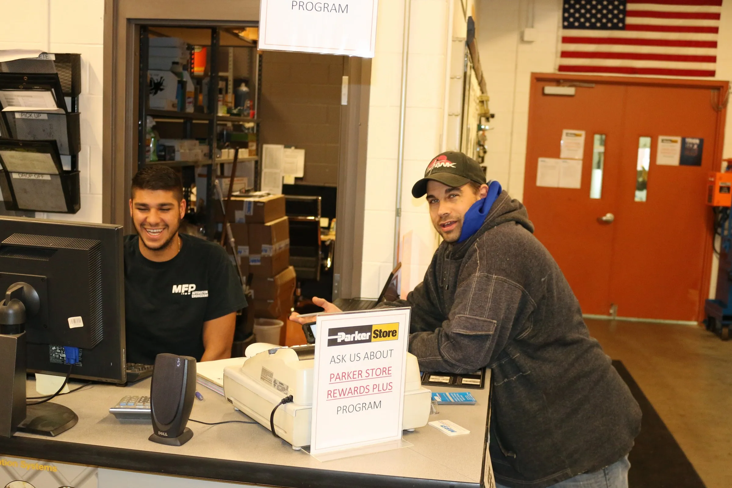 A staff member in an MFP shirt helps a customer at the ParkerStore counter, both smiling