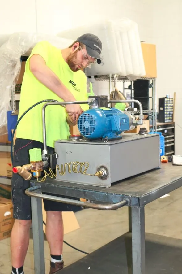 Worker wearing an MFP shirt assembling a blue WEG motor onto a hydraulic reservoir at a workbench