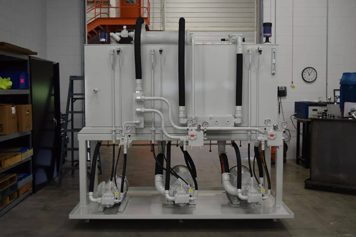 Grey three-motor hydraulic power unit with piped reservoir and gauges in a shop