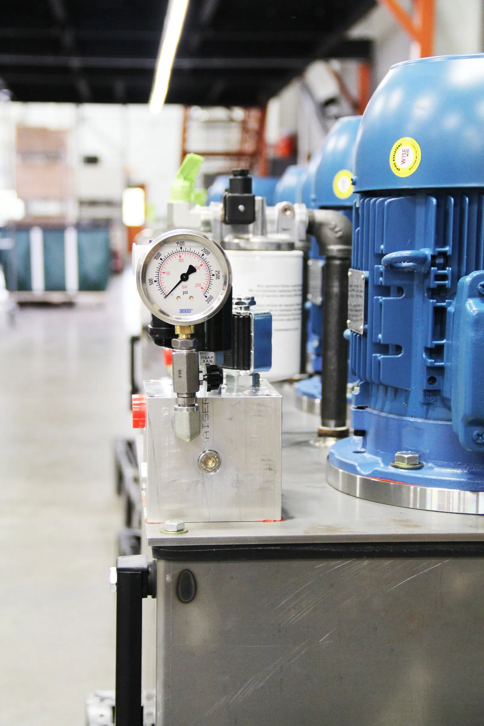 A row of identical small hydraulic power units with blue motors and pressure gauges