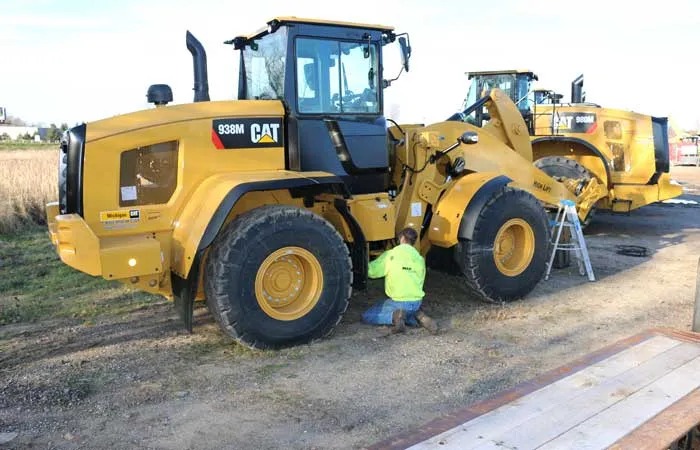 Technician kneeling beside a Caterpillar wheel loader during an on-site installation