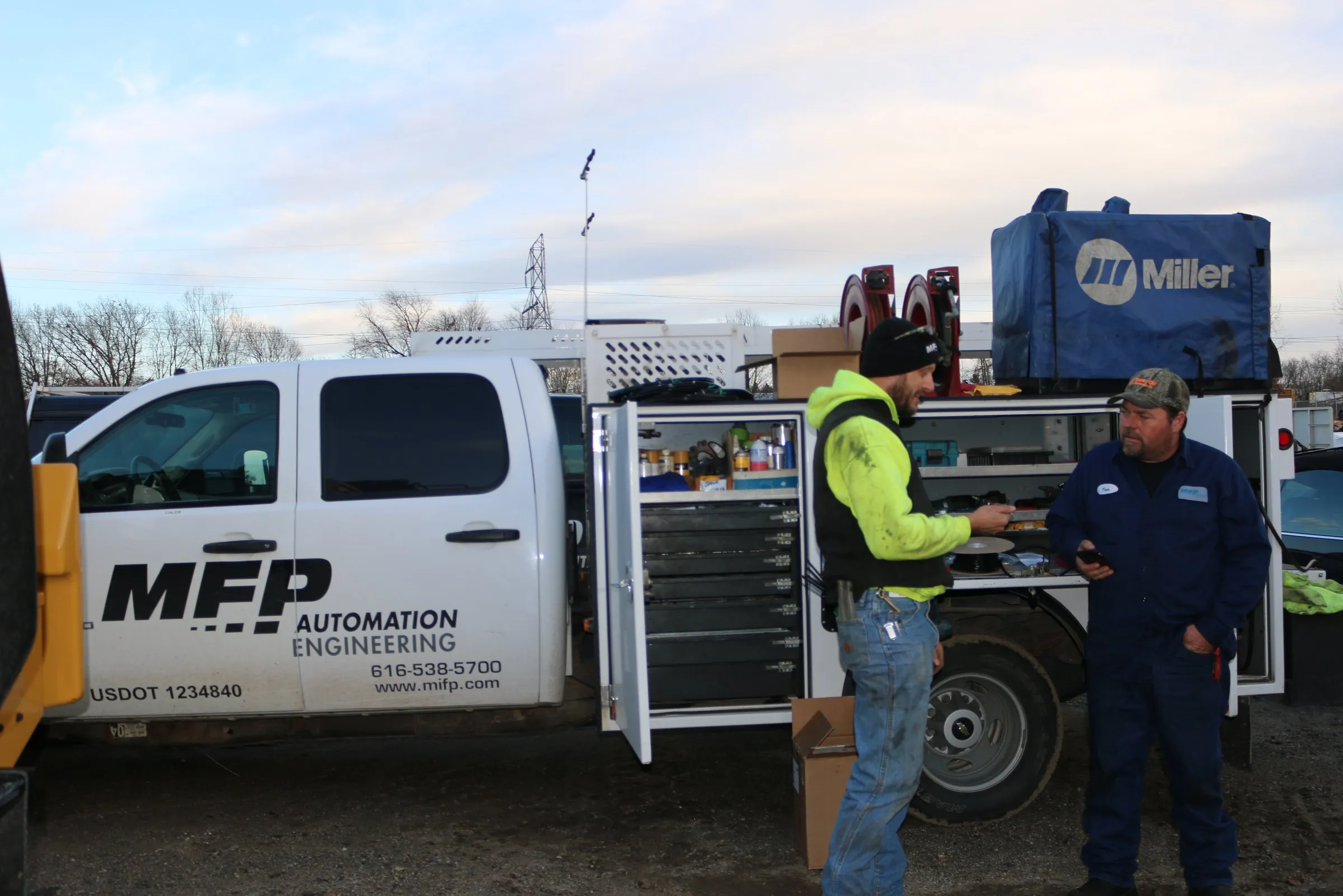 Two technicians talking beside an MFP service truck on an outdoor job site at dusk