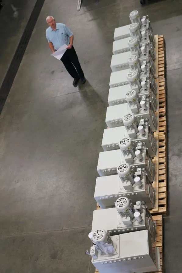 An overhead view of a long row of hydraulic power units on a shop floor, with a worker reviewing paperwork beside them