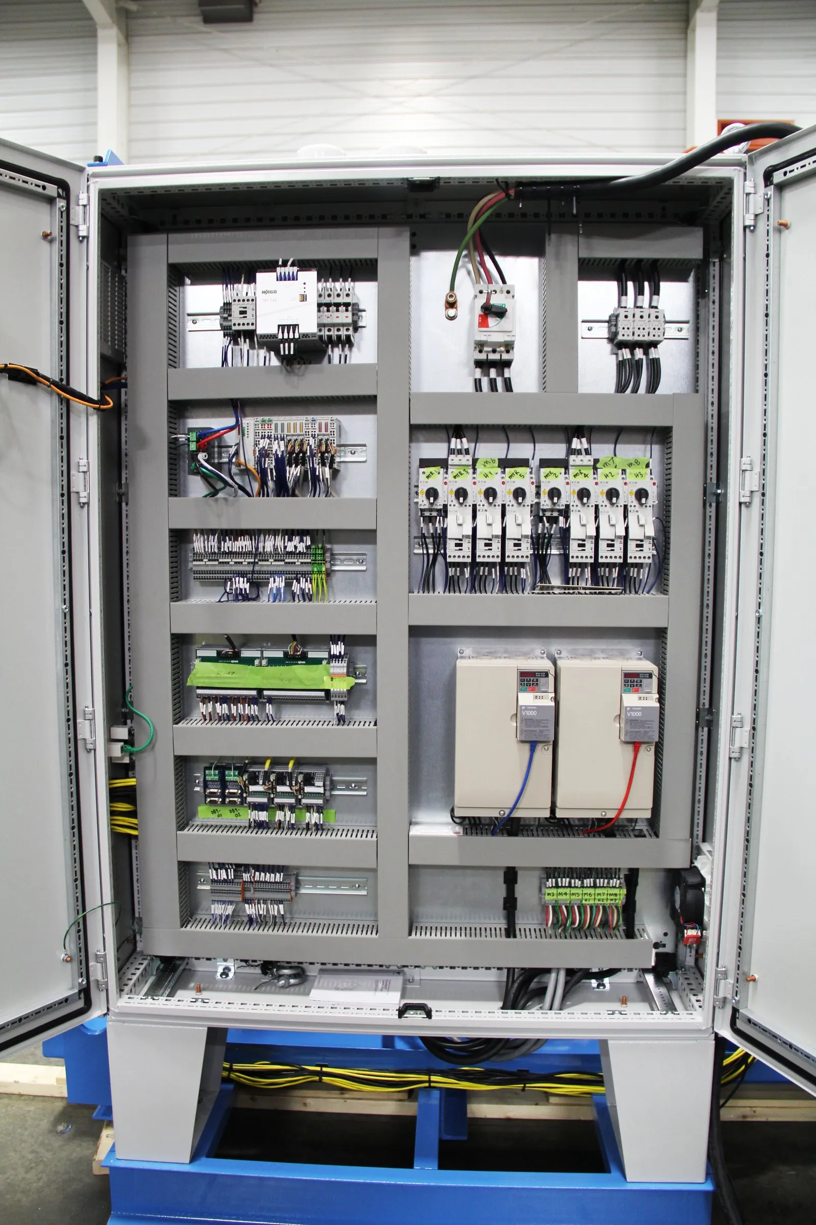 Open gray electrical control cabinet with breakers, terminal blocks, relays and drives