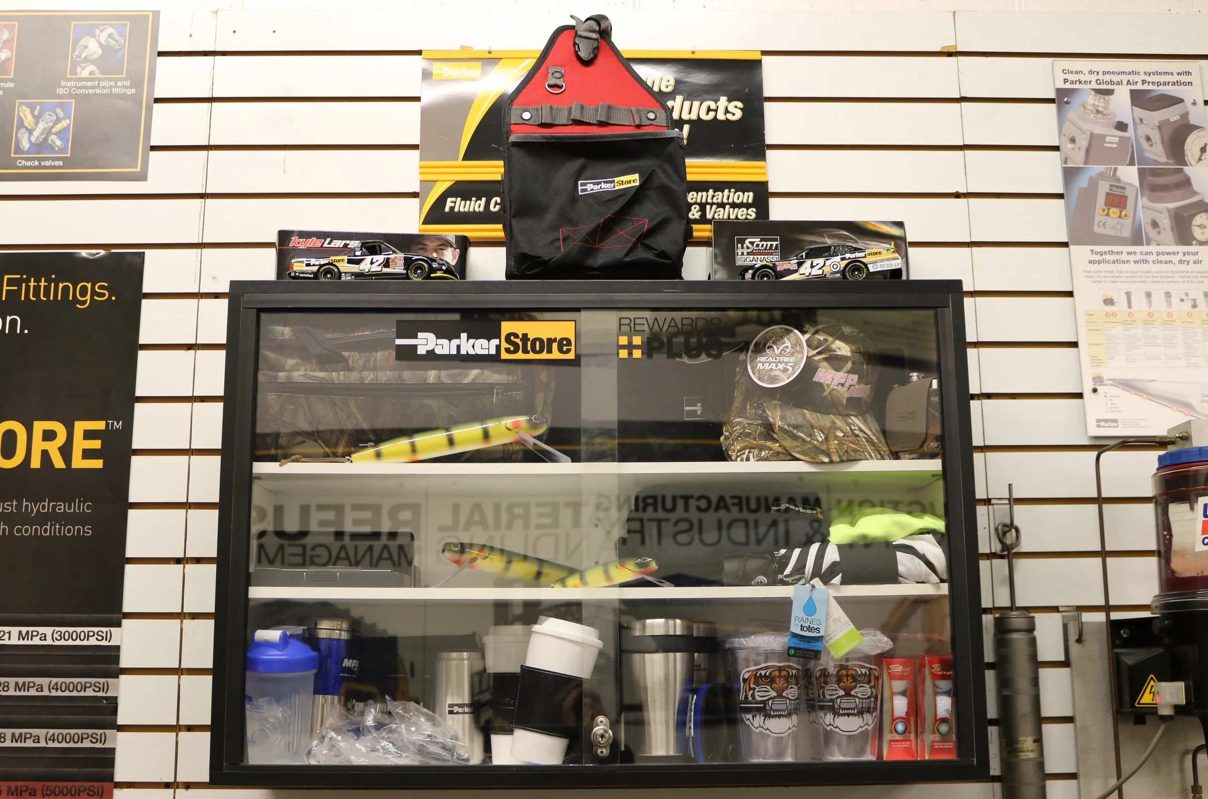 A ParkerStore display case shows fishing lures, tumblers and a camo cap beneath Rewards Plus signage