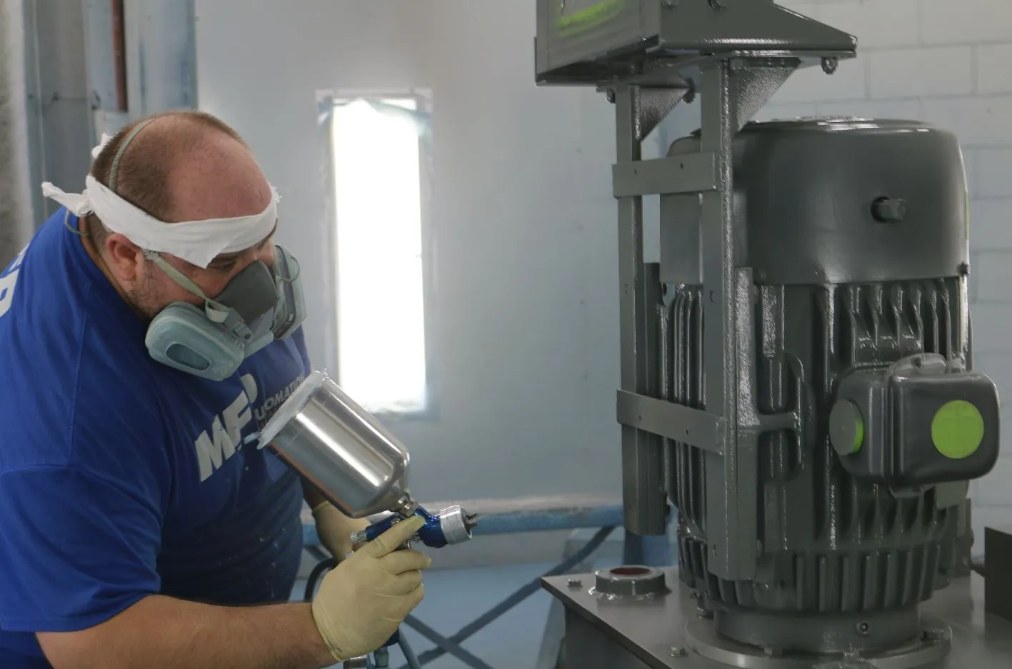 MFP technician in a respirator spray-painting a power unit motor in the paint booth
