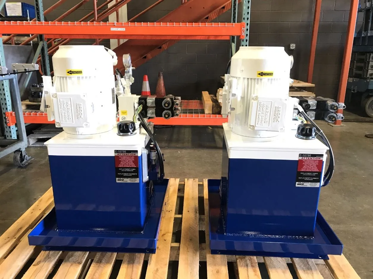 Two hydraulic power units on a pallet, each carrying a tag reading "For Service Contact: MFP"