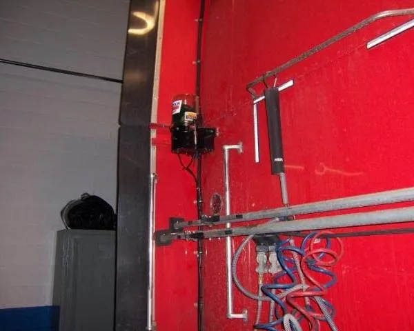 A small hydraulic pump and coiled hoses mounted inside a red trailer door or lift gate