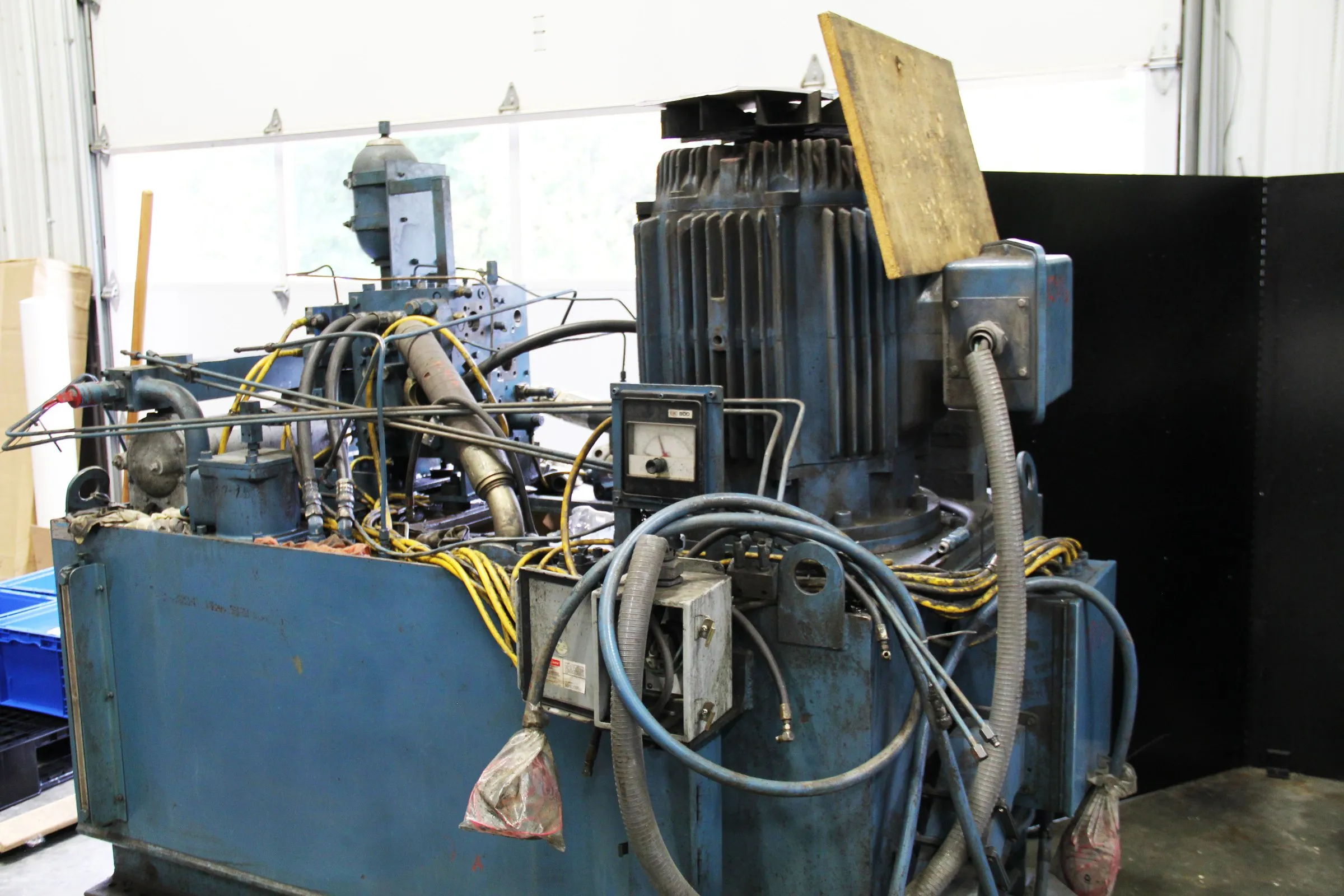 Worn blue industrial hydraulic power unit with oily hoses and junction boxes, in for repair
