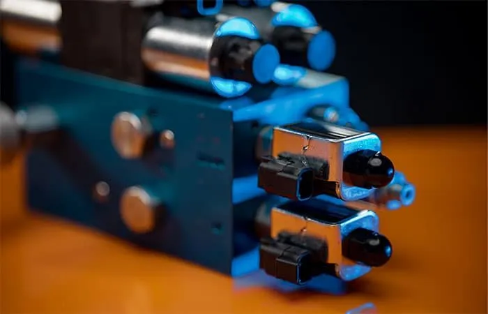 Blue-anodized solenoid valve manifold with electrical connectors, shown in a lit product photo