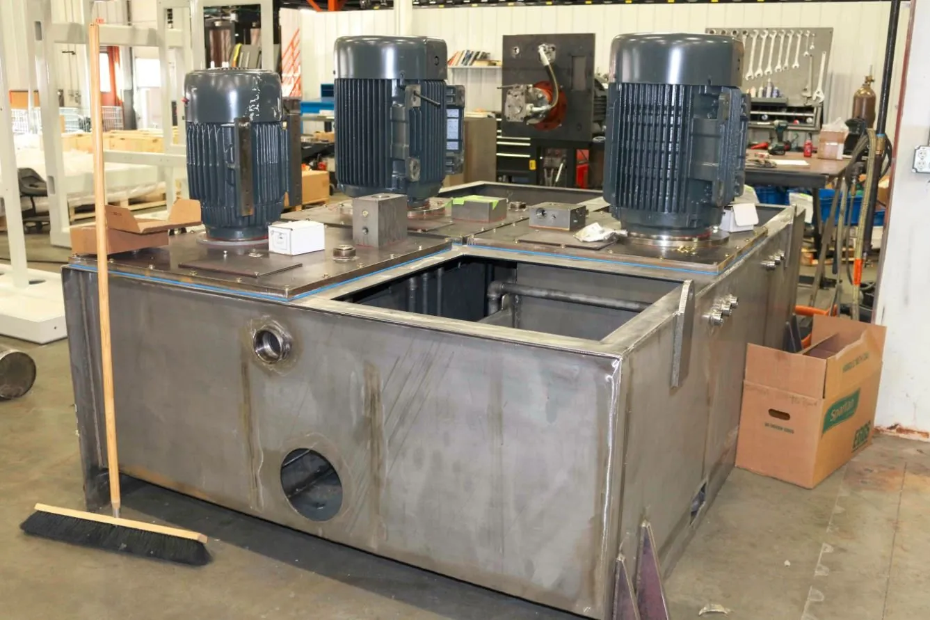 Stainless steel reservoir with three large motors mounted on top, mid-fabrication in a shop