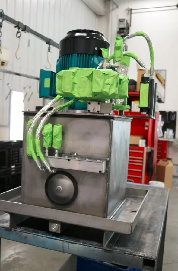 Small teal-painted motor wrapped in green protective tape, mounted on a stainless hydraulic reservoir on a cart