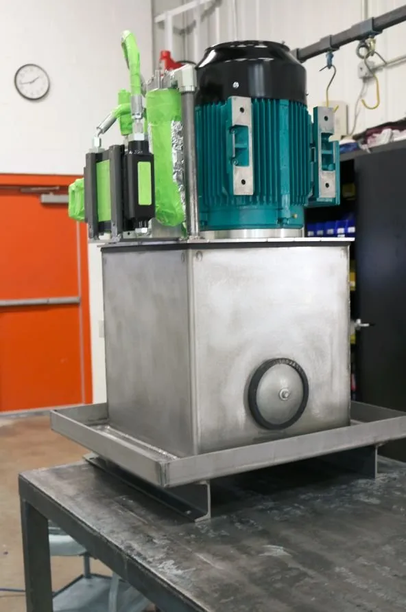 Teal-painted motor wrapped in green protective tape, mounted on a stainless hydraulic reservoir, near an orange door