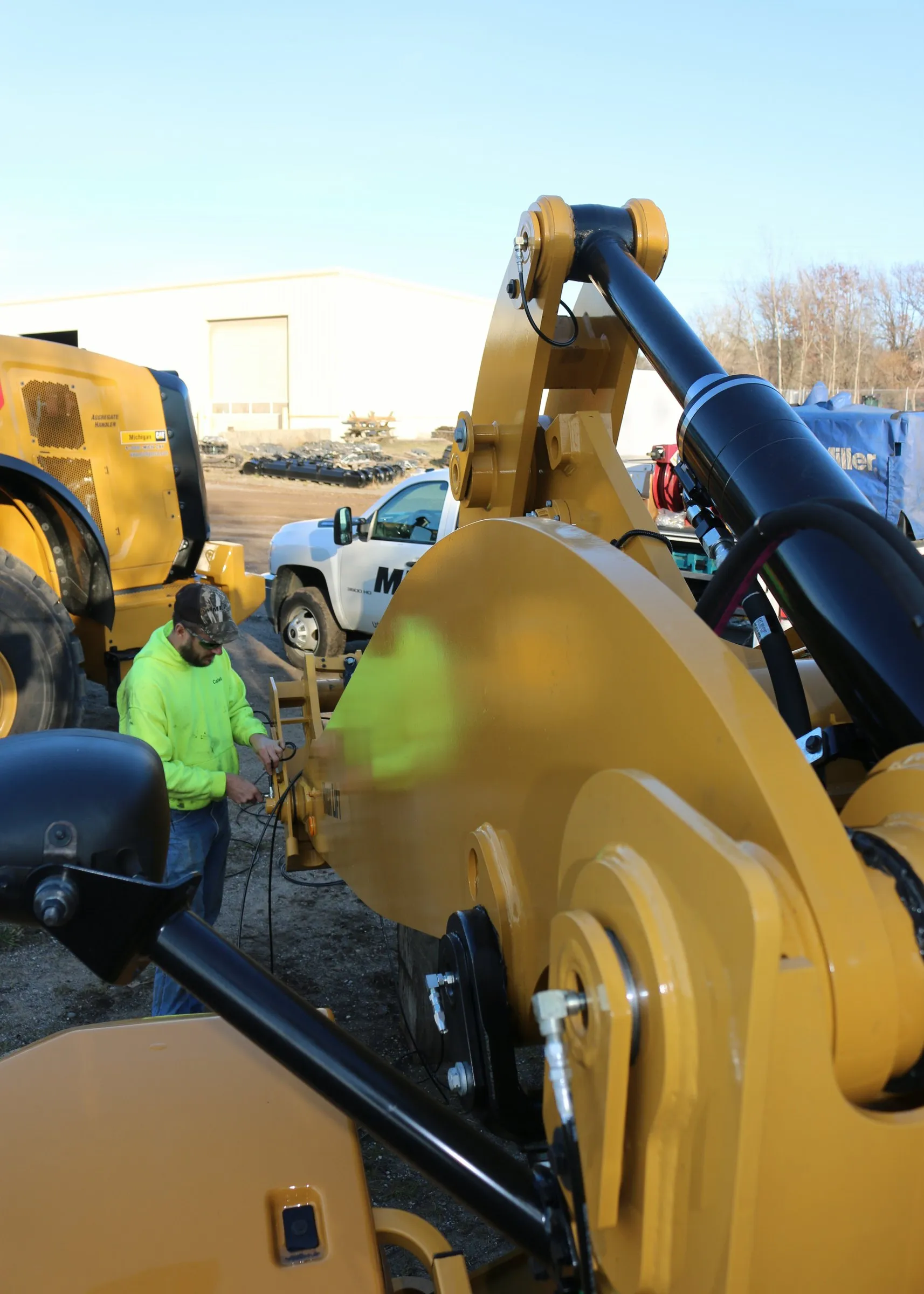 Technician in a hi-vis hoodie working near the boom of a yellow Caterpillar wheel loader outdoors