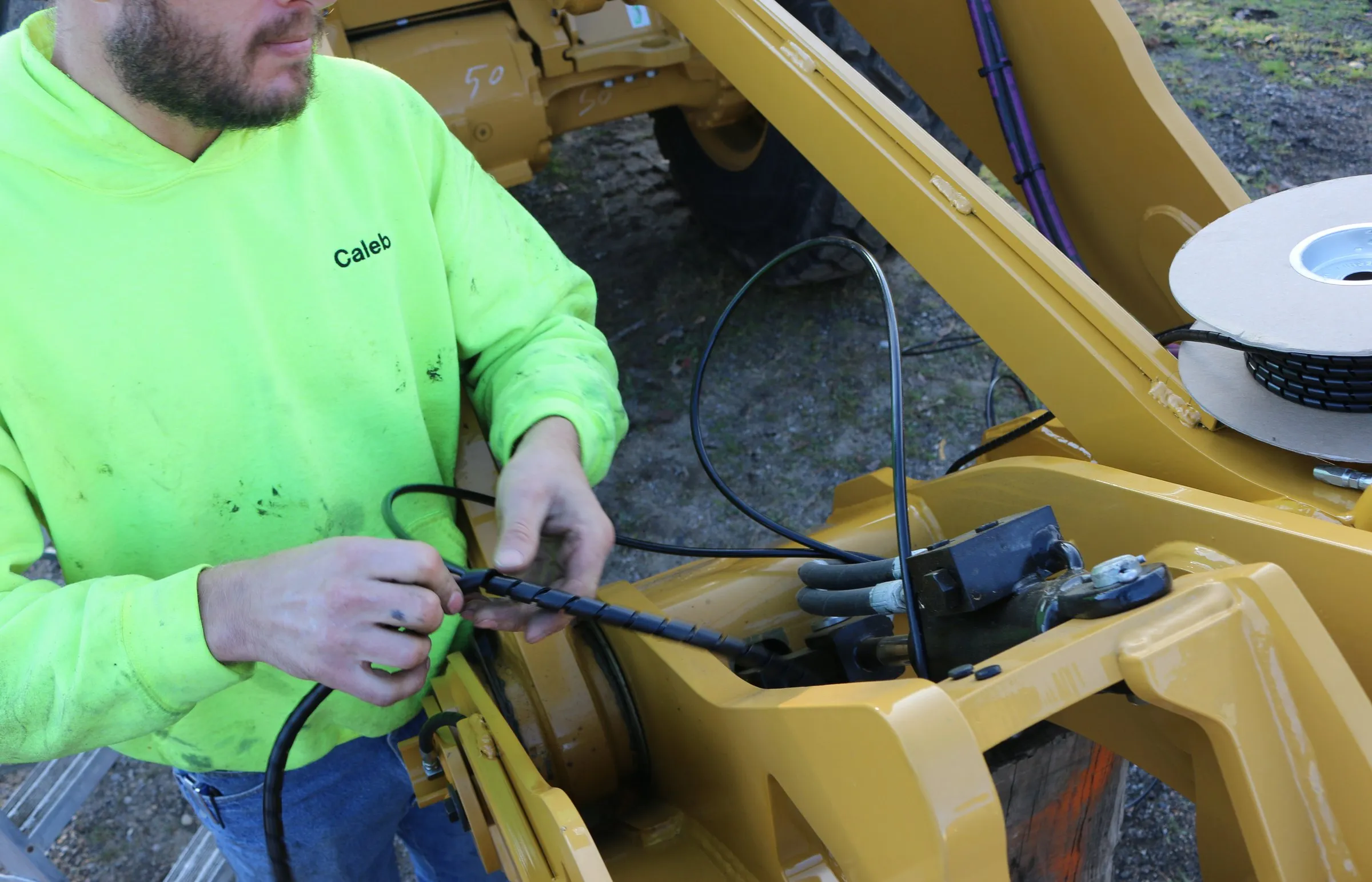 Technician handles a hydraulic hose beside a wire spool on a wheel loader