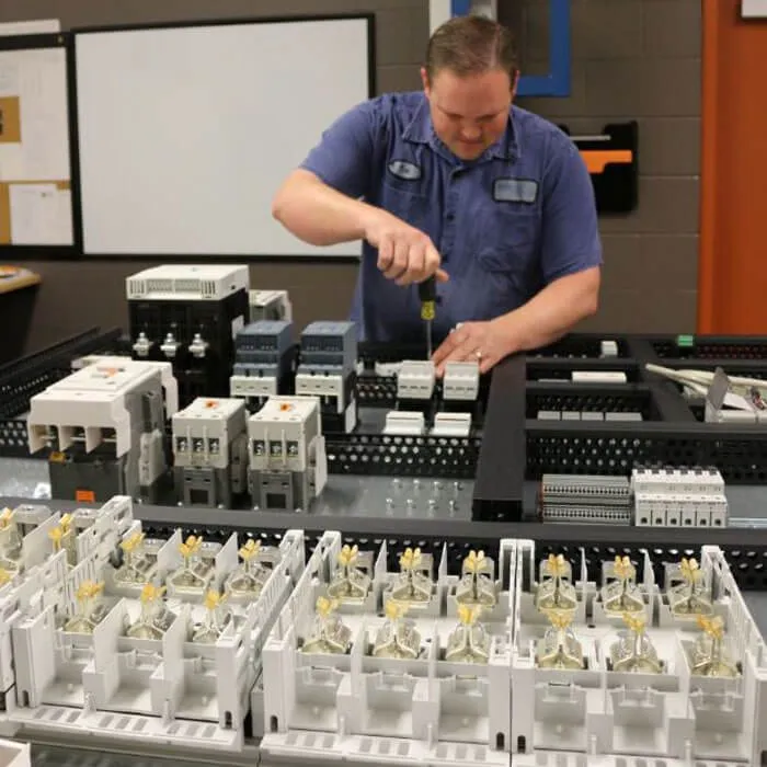 A technician wires breakers and terminal blocks into a control panel at a workbench