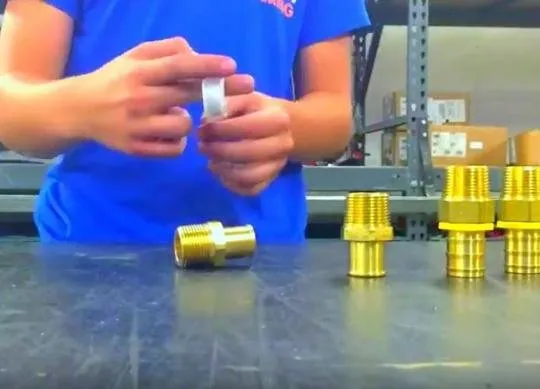 Person in an MFP shirt wrapping thread tape on a brass pipe fitting at a workbench