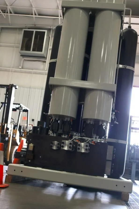 Two large cylindrical accumulators mounted on a steel frame in a warehouse, with a forklift and safety cone nearby