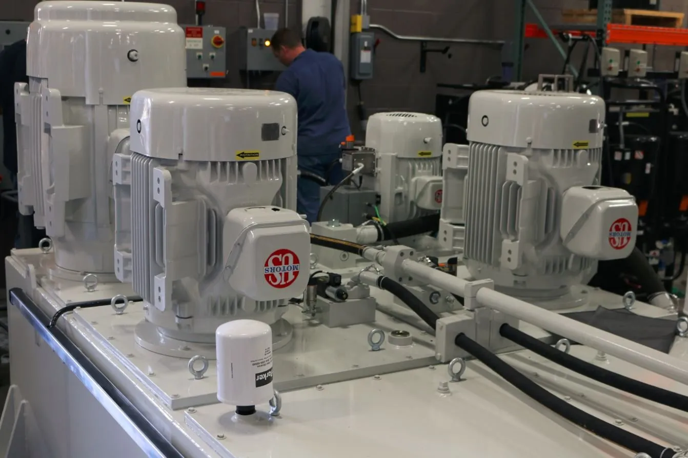Row of white motors marked US Motors and a Parker filter mounted on a hydraulic power unit, with a worker in the background