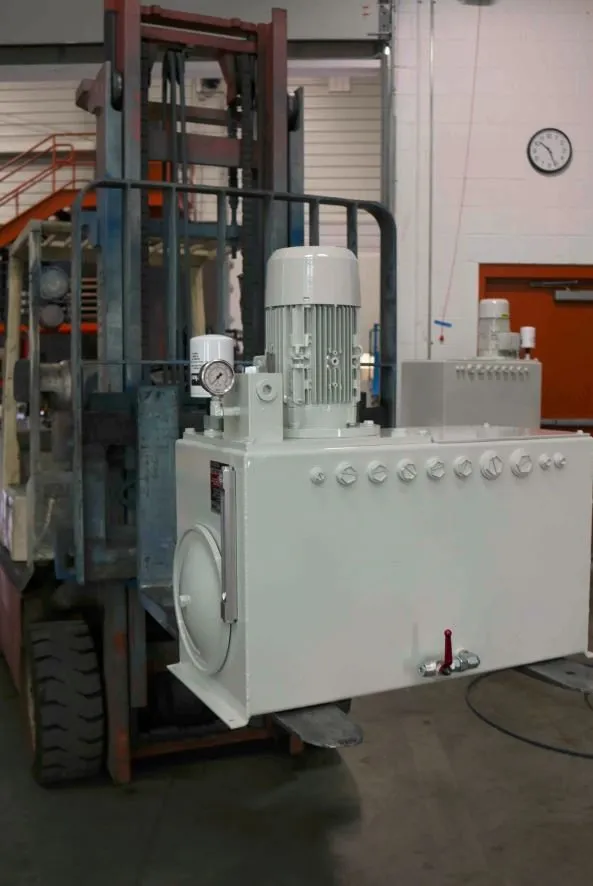 White hydraulic power unit with a motor and gauge, loaded on the forks of a red forklift near a wall clock