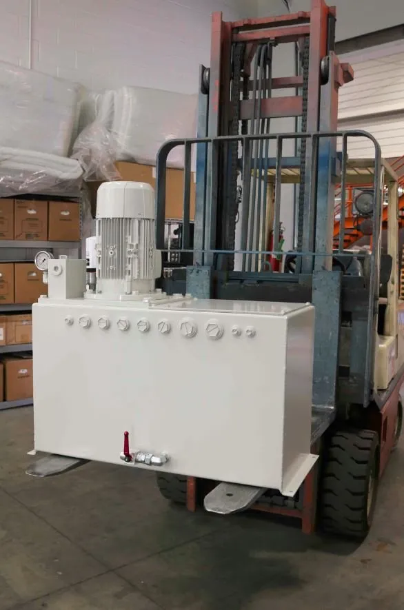 White hydraulic power unit with a motor and gauge, loaded on the forks of a red forklift in a warehouse
