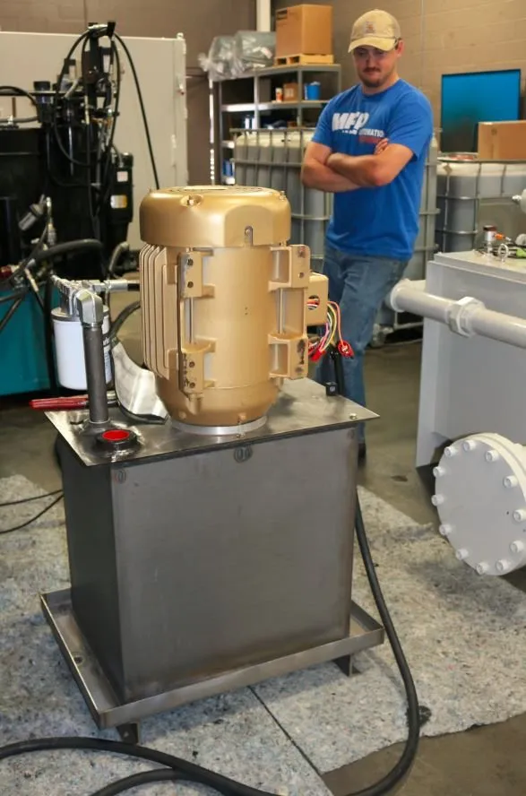 A worker in an MFP Automation shirt stands with arms crossed beside a gold motor mounted on a hydraulic tank